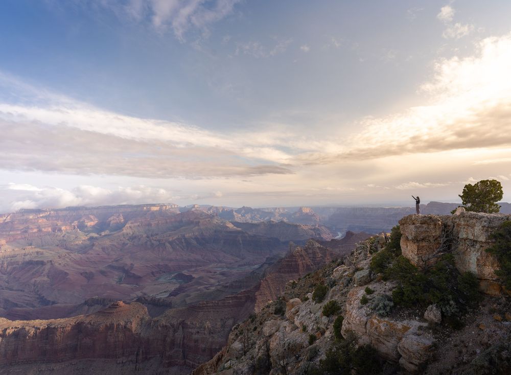 Panoramic view of the Grand Canyon's red rock formations and deep valleys stretching to the horizon at sunset.
