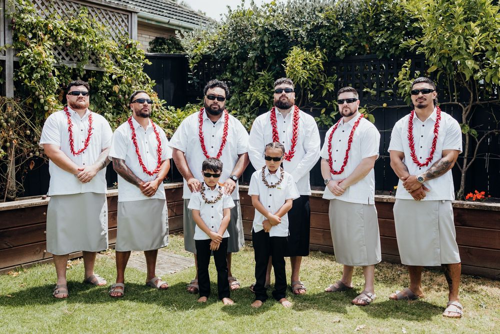 Wedding party group wearing white shirts with red leis posing together outdoors.