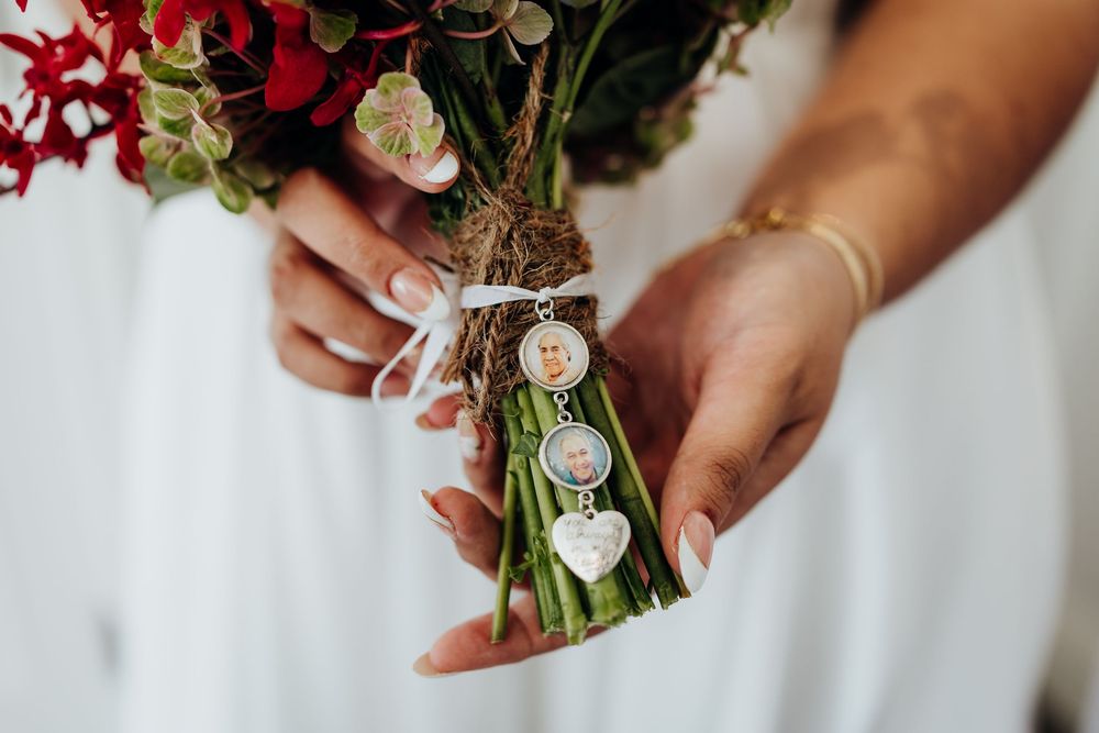 Close-up of hands holding red and white wedding bouquets with decorative charm attachments.