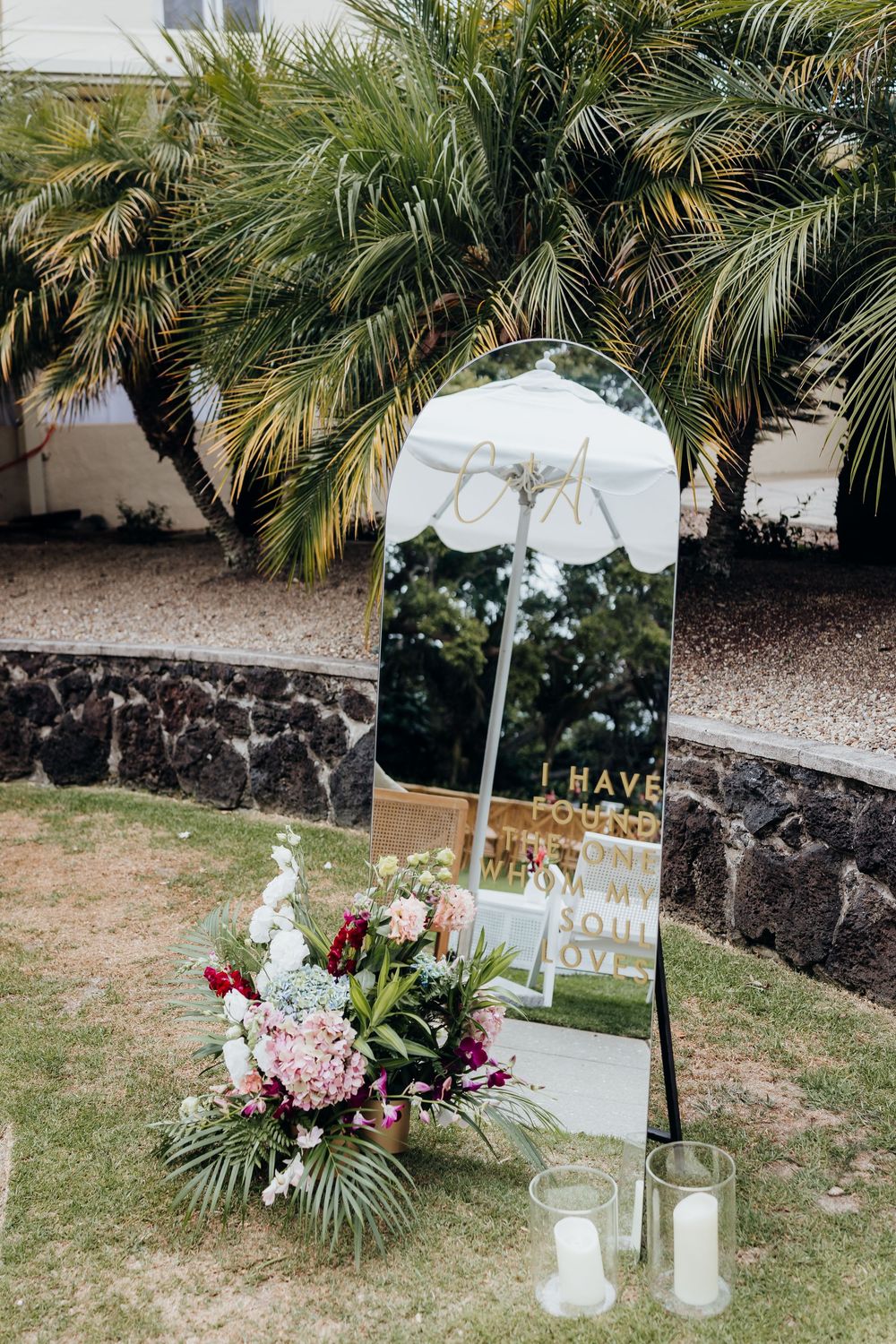 Romantic outdoor wedding setup with white signs and floral arrangements against a tropical palm backdrop.