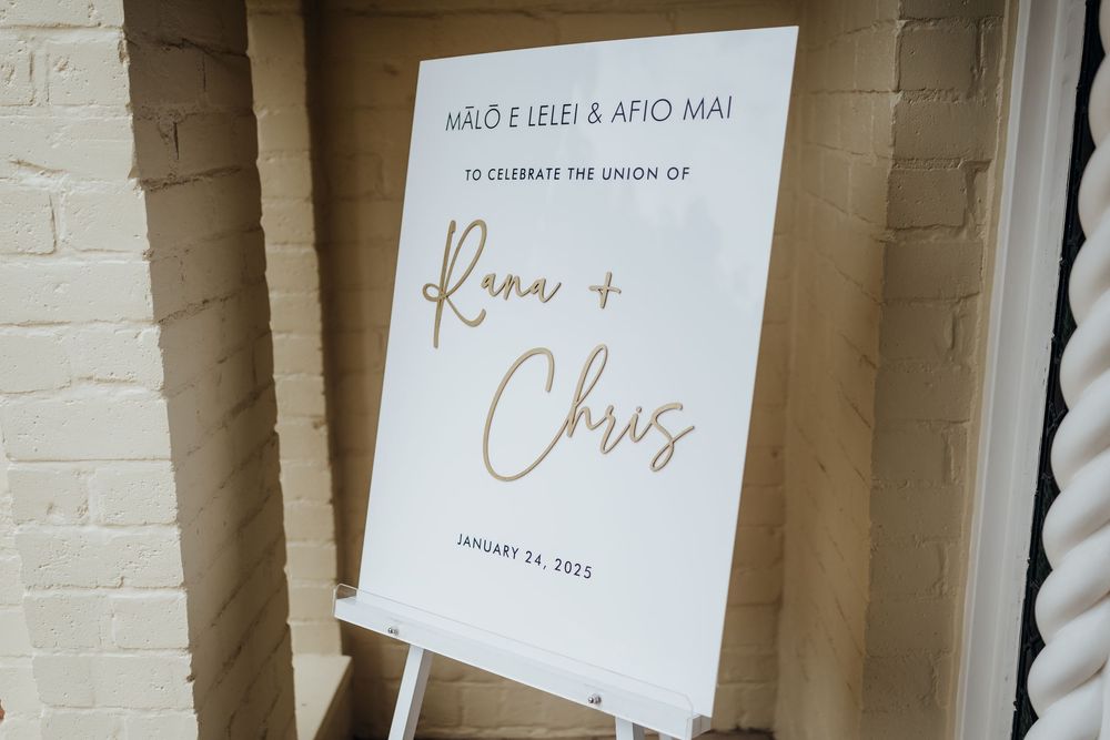 Elegant wedding signage with gold lettering displayed against a white brick wall.