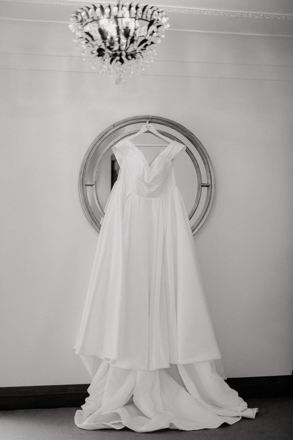 A white wedding dress hangs elegantly against a light-colored wall beneath ornate ceiling decorations.