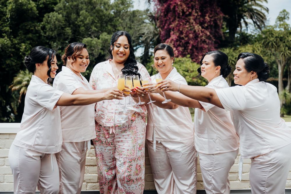 Wedding party group in white attire posing together in a celebratory moment outdoors.