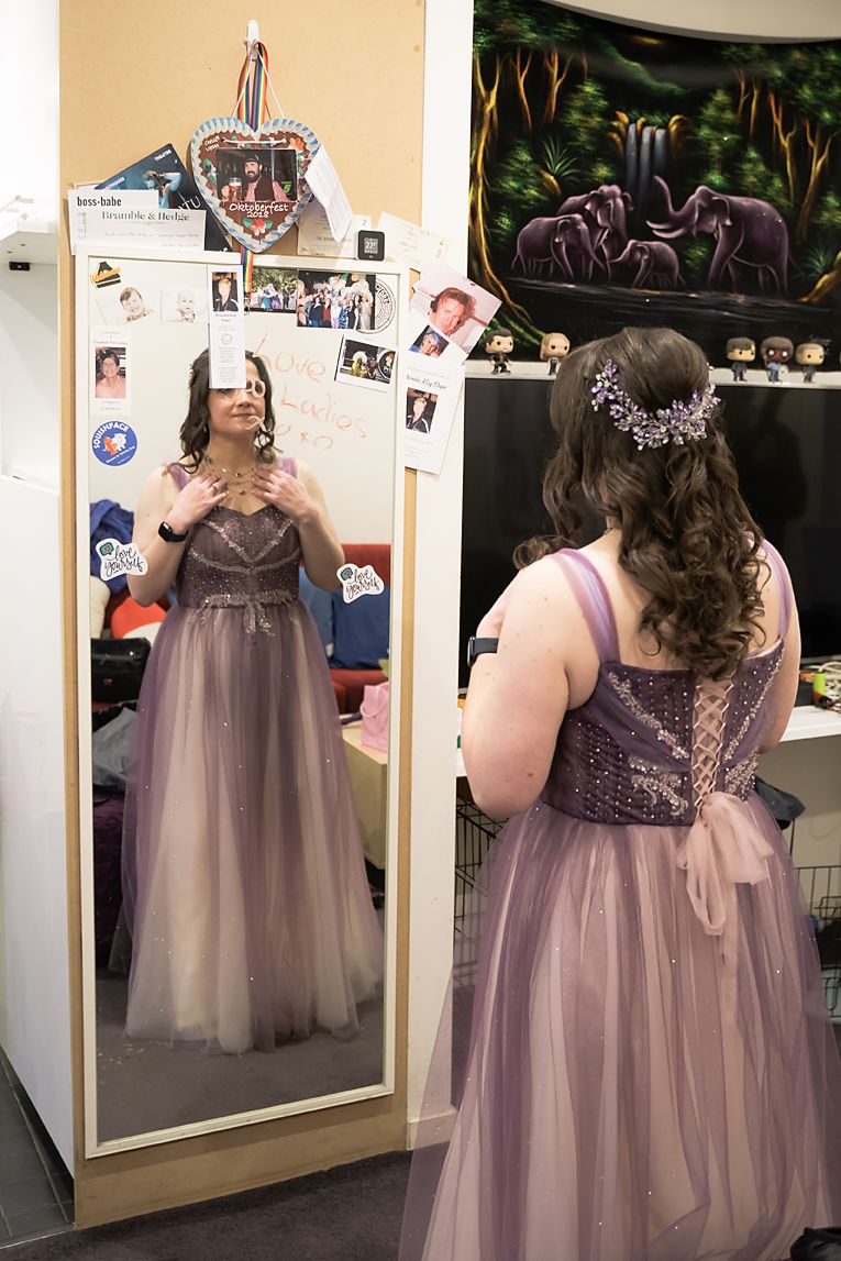 A person in a lavender tulle gown admires their reflection in a dressing room mirror while getting ready.