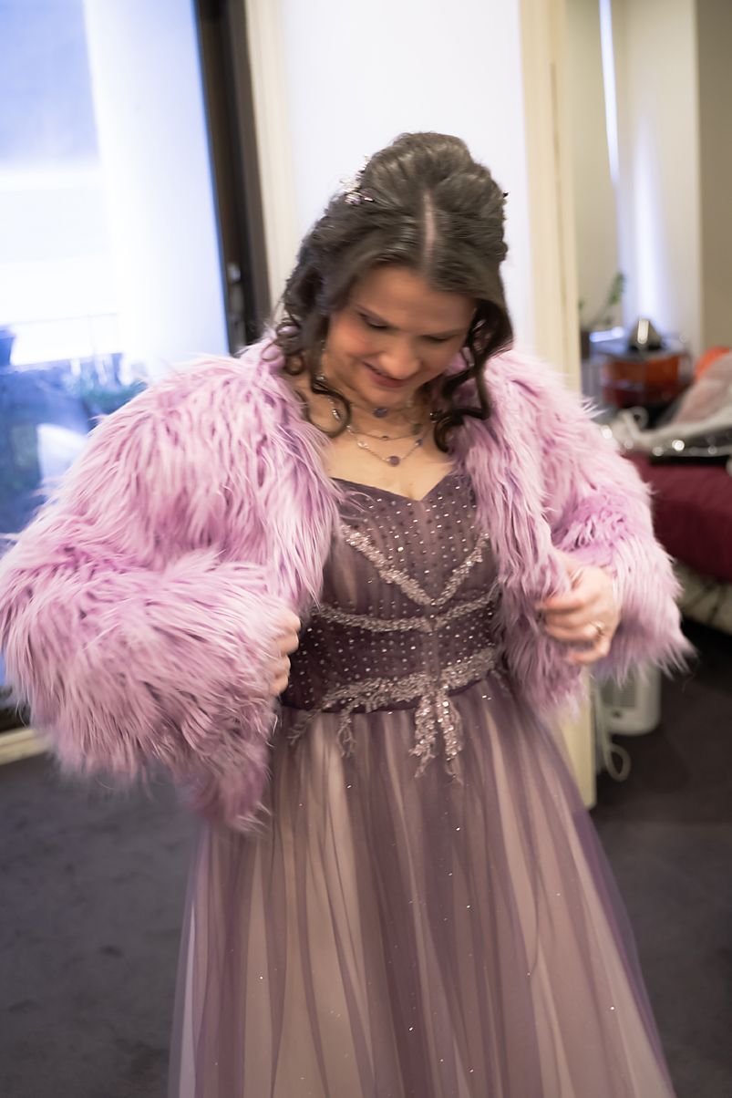 A person in a sparkly purple dress and pink fluffy jacket twirls while dancing.