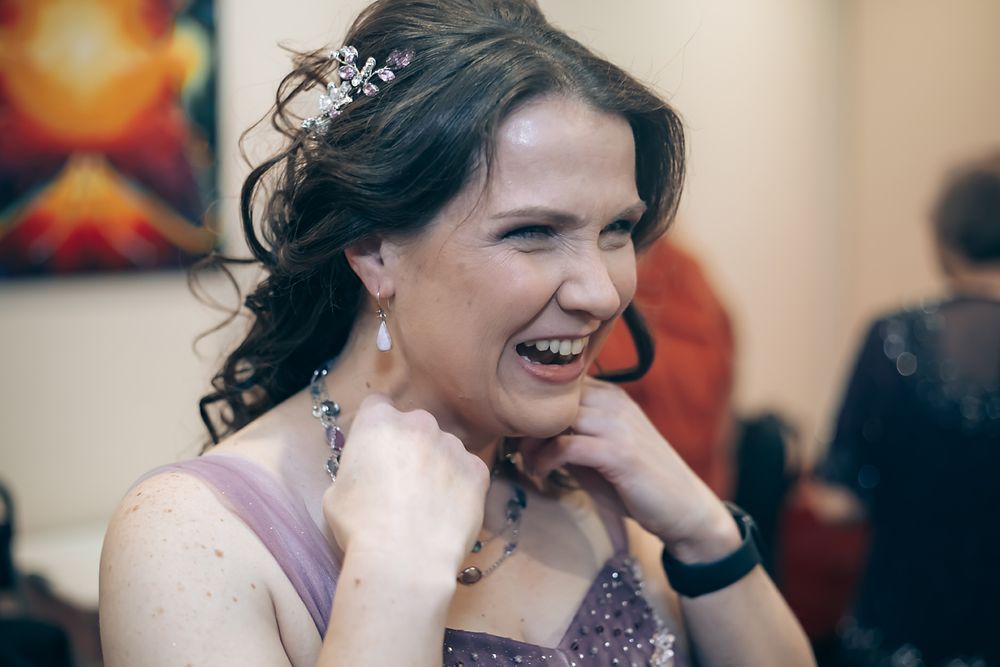 A smiling person in a purple evening gown poses with sparkly jewelry at a formal event.