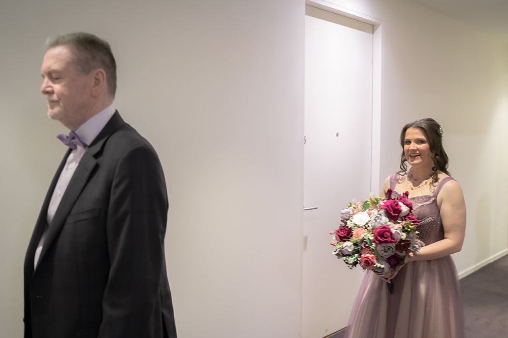 A wedding party member in formal attire walks together in the hallway holding a colorful bouquet.