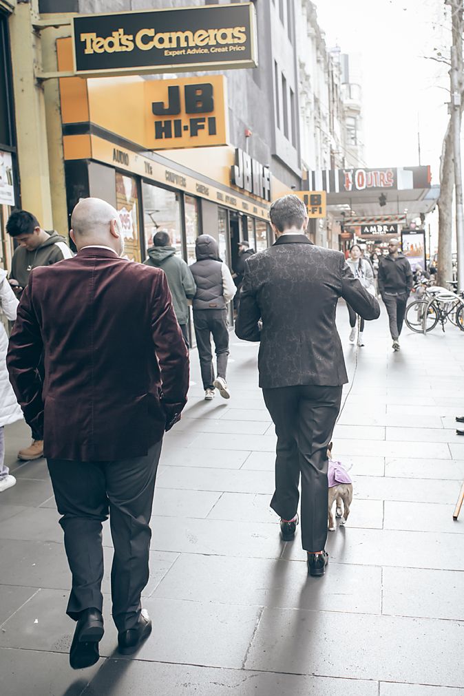 People walking on a busy street past Ted's Cameras and JB HiFi storefronts in an urban setting.