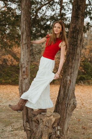 Someone wearing a white t-shirt and jeans sits casually on a bed with a ring light visible in the background.