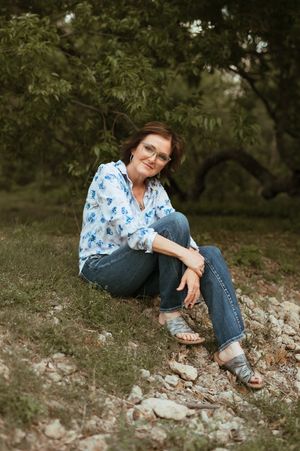 Outdoor portrait showcasing a floral print top and blue jeans while seated on rocky terrain under leafy trees.