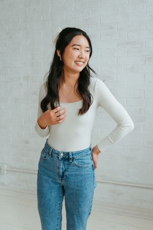 Casual portrait against white brick wall showing person wearing white long sleeve top and classic blue denim jeans.