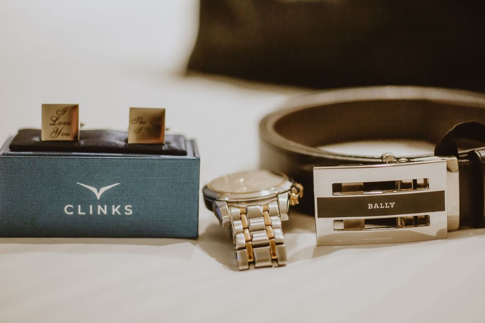 Luxury leather accessories including watch bands, wallets, and cufflinks arranged on a neutral beige surface.