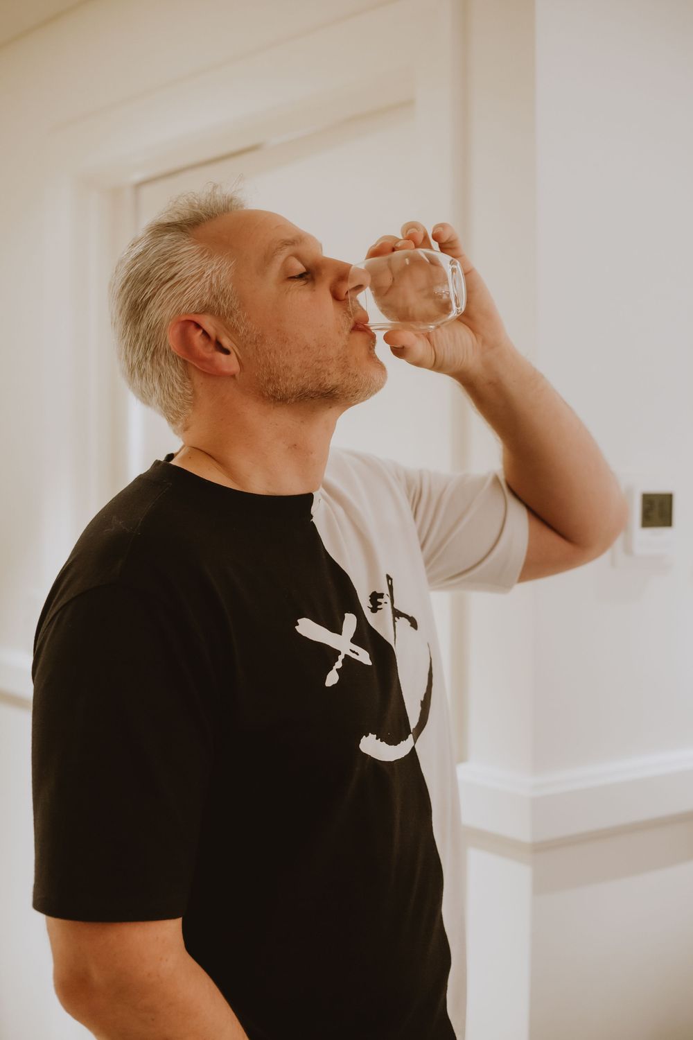 A person in a black t-shirt taking a drink from a glass in a sequence of movements.