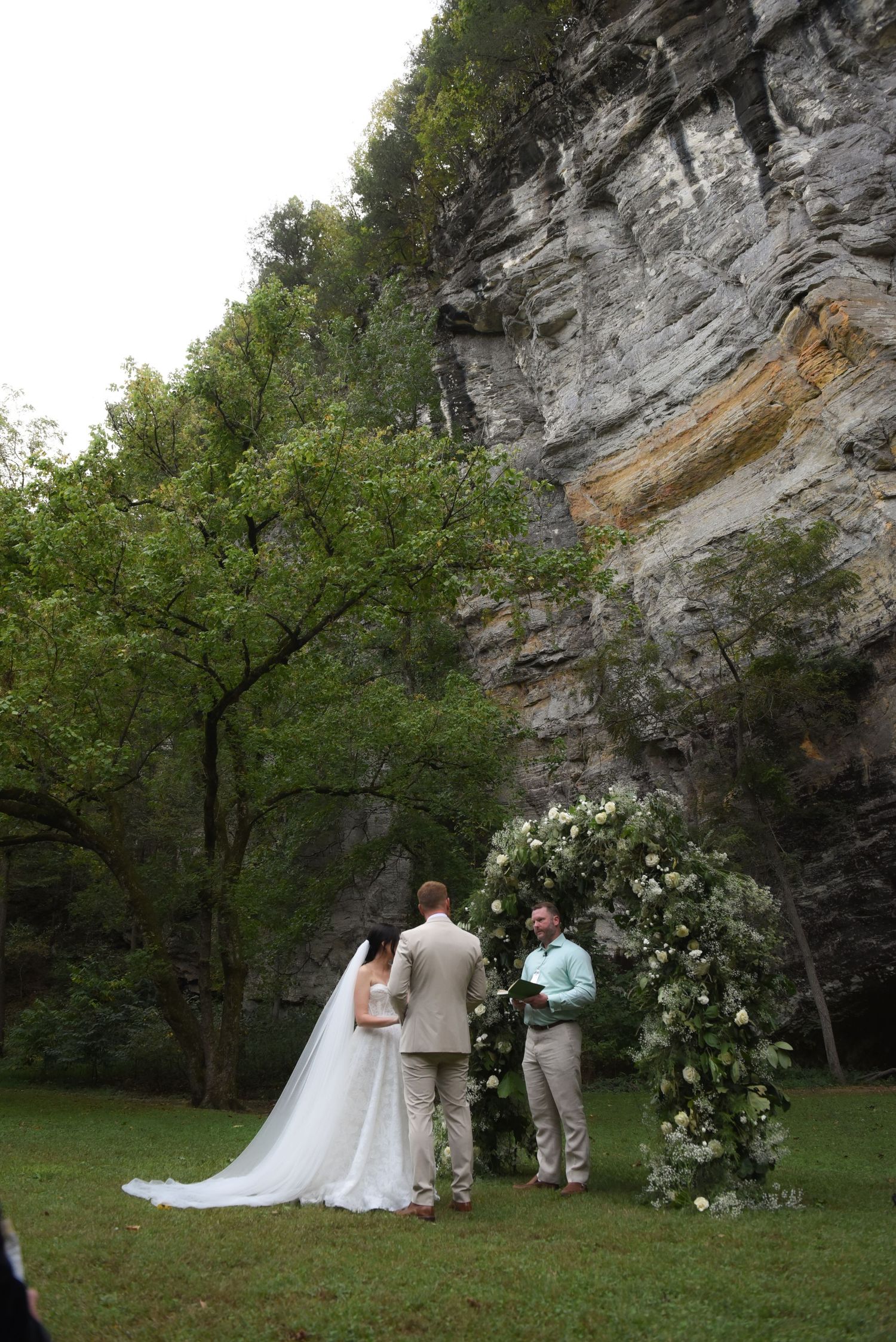Wedding ceremony setup in a natural amphitheater with limestone cliffs and white flowers.