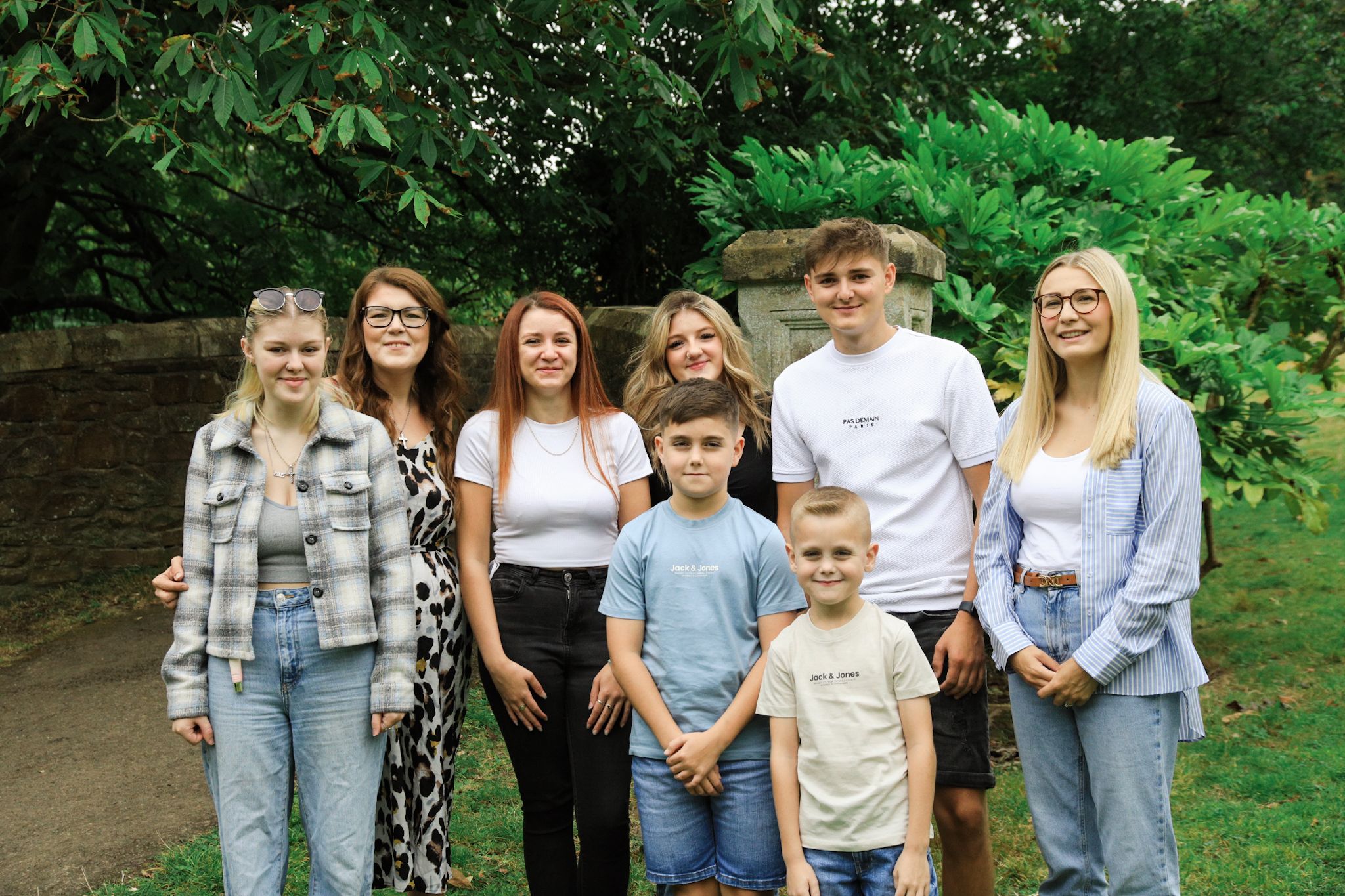 A group stands together outdoors in a garden setting with lush green foliage in the background.