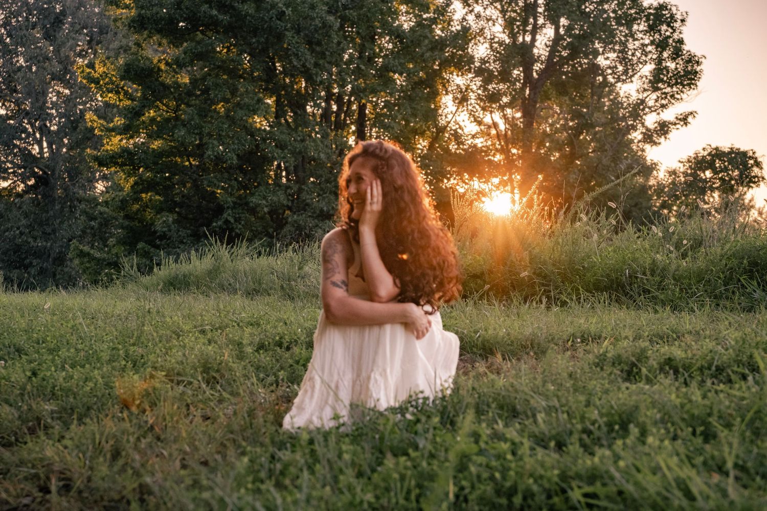 Golden sunlight illuminates a romantic scene in a grassy field with trees in the background.
