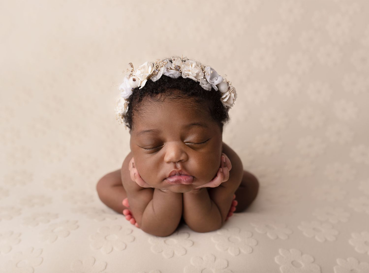 Sweet newborn baby sleeping peacefully on cream-colored blanket in professional studio setting.