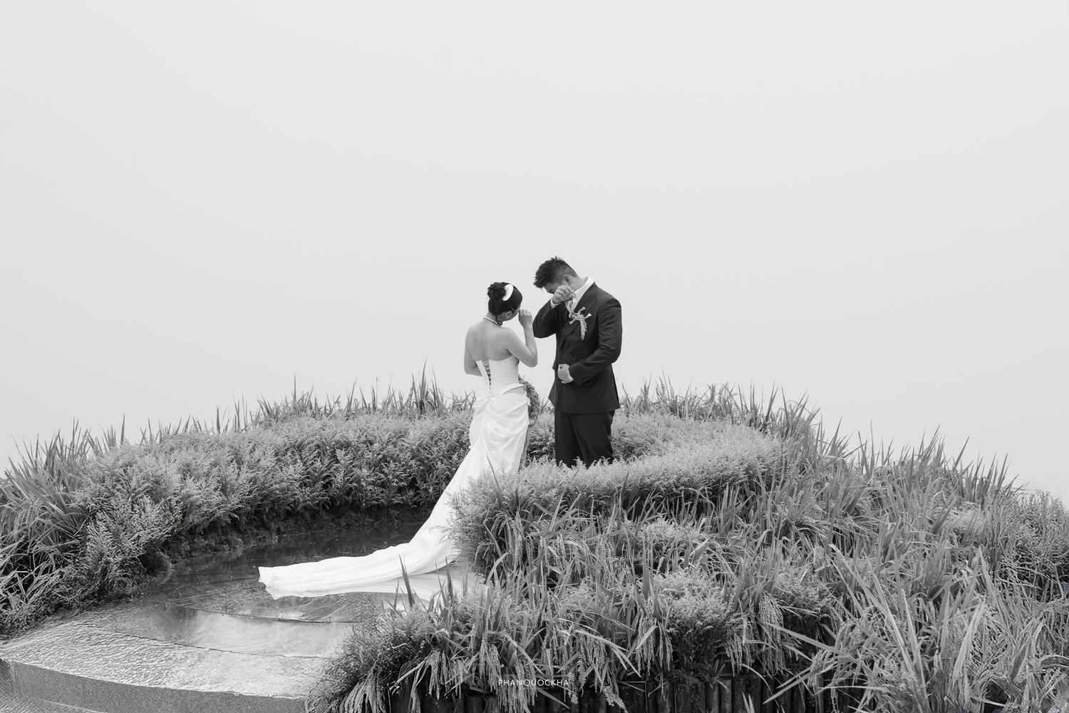 Black and white artistic wedding photo of couple sharing intimate moment on misty green hillside pathway.
