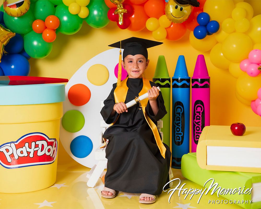 Playful graduation scene with educational toys, balloons and decorative elements against yellow background.
