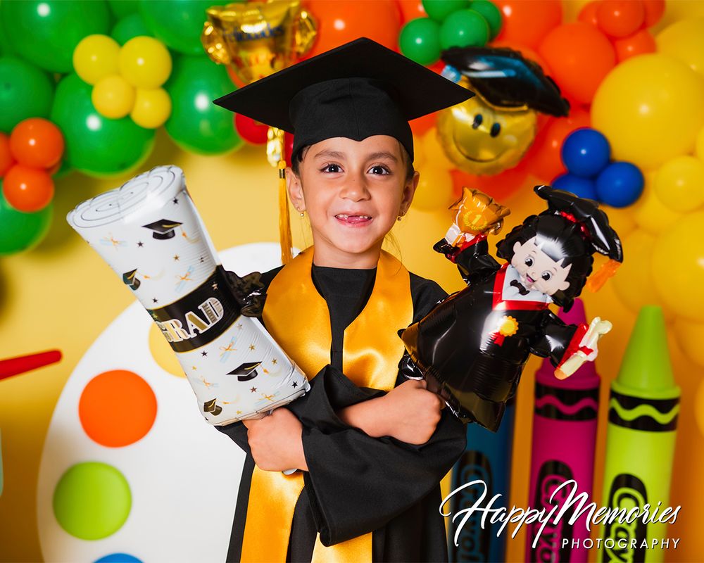 Playful graduation photo backdrop with cap and gown theme surrounded by balloon garland and props.