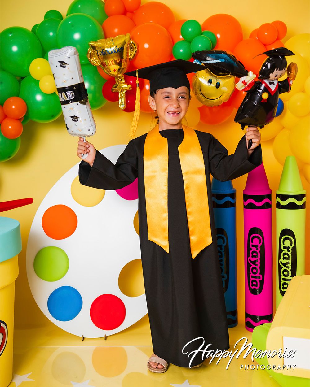 Graduation photo display with oversized crayons, Play-Doh containers, and festive balloons in bright colors.