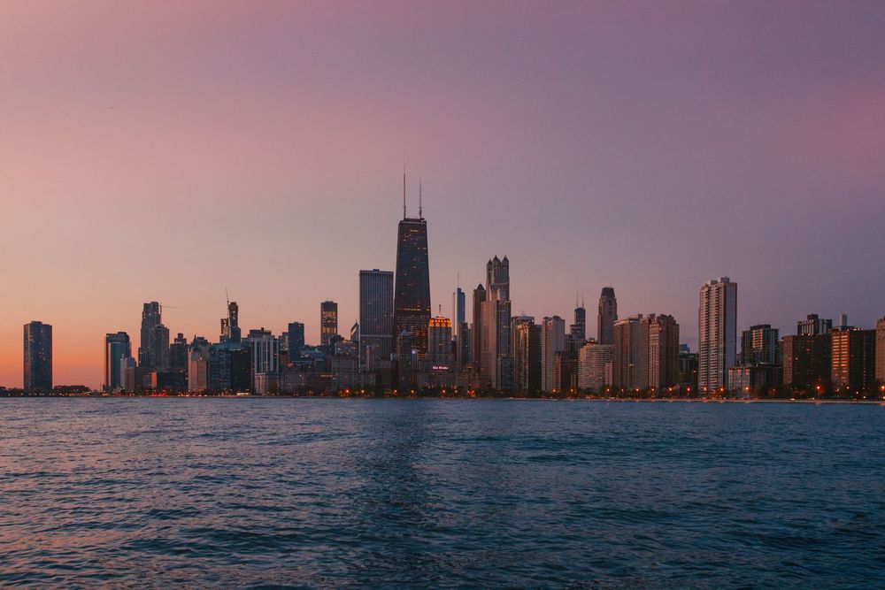 Chicago skyline silhouetted against pink and orange sunset over Lake Michigan.