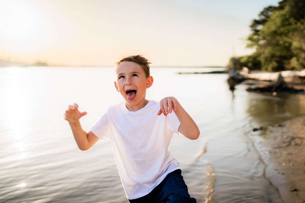A person wearing a white shirt and khaki shorts walks along the shoreline of a scenic beach at sunset.