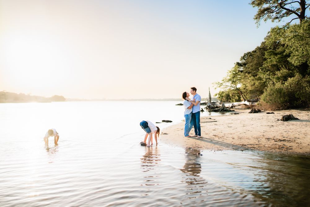People enjoying a peaceful evening walk along a tranquil lakeside beach as the sun sets over the water.