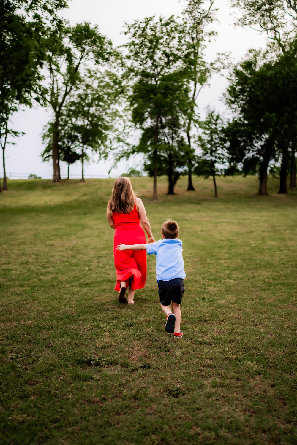 A pair of people in red and blue clothing walk together across a grassy hillside on a summer afternoon.