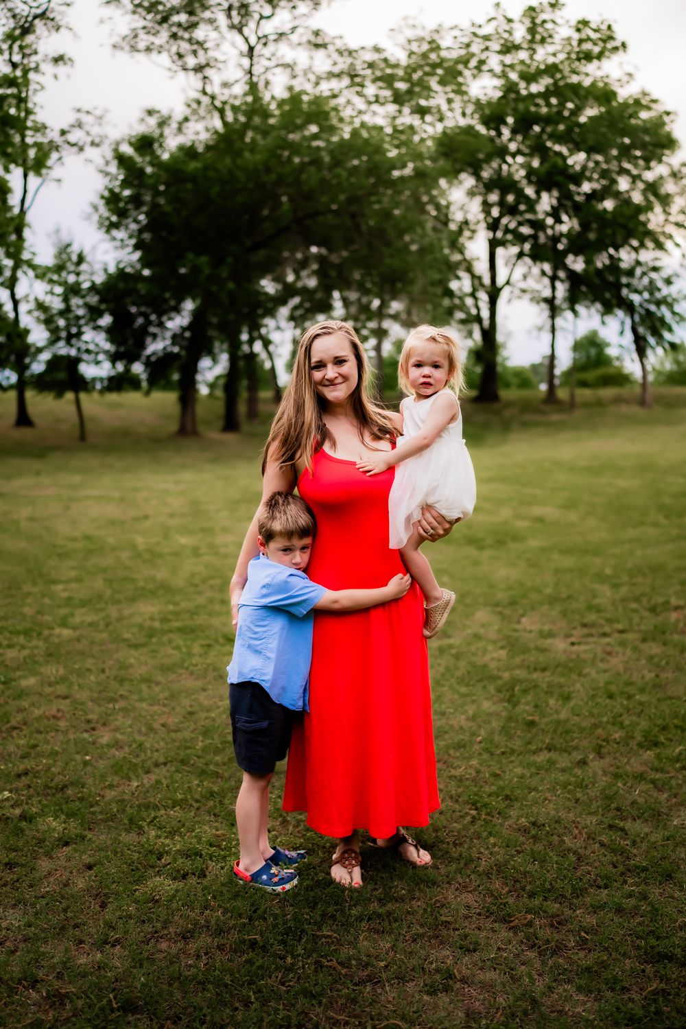 Three candid outdoor photos show a sweet embrace between a figure in a bright red dress and a child in blue on grassy ground.