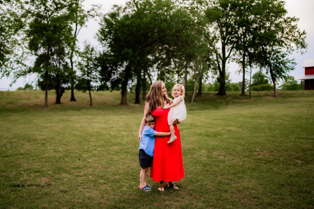 A family explores a grassy meadow together on a sunny day surrounded by leafy green trees in the distance.