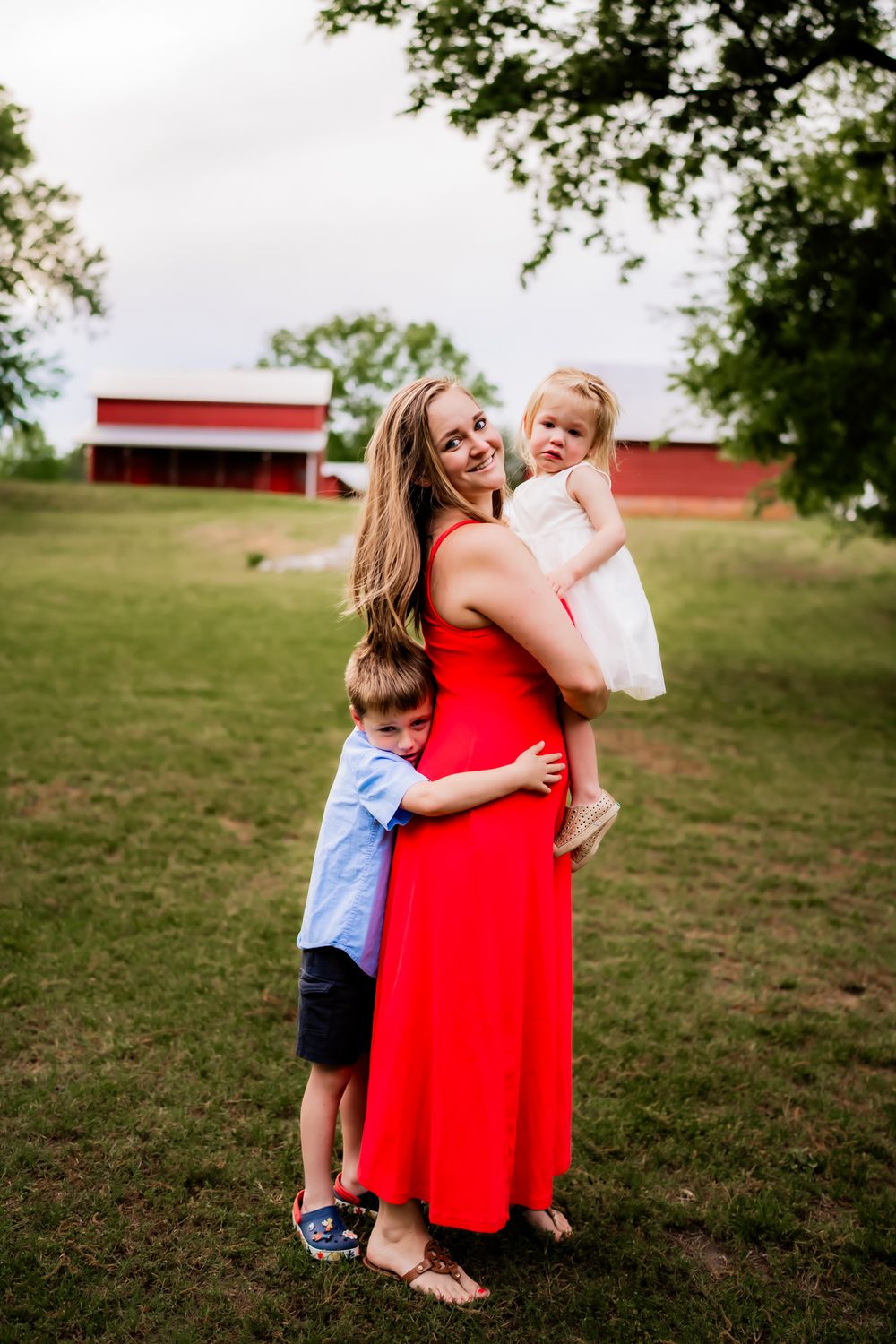 A family shares joyful moments together on a grassy hill with a red barn in the background on a summer day.