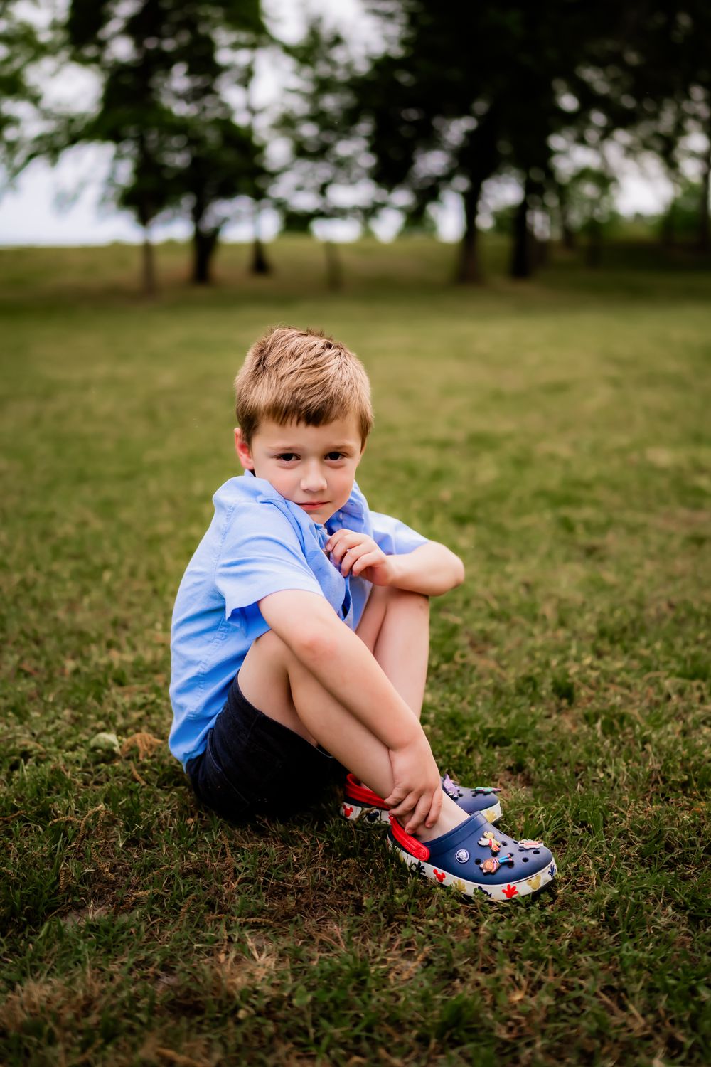 Child sits in blue shirt and shorts on grassy hill in three similar poses captured from different angles.