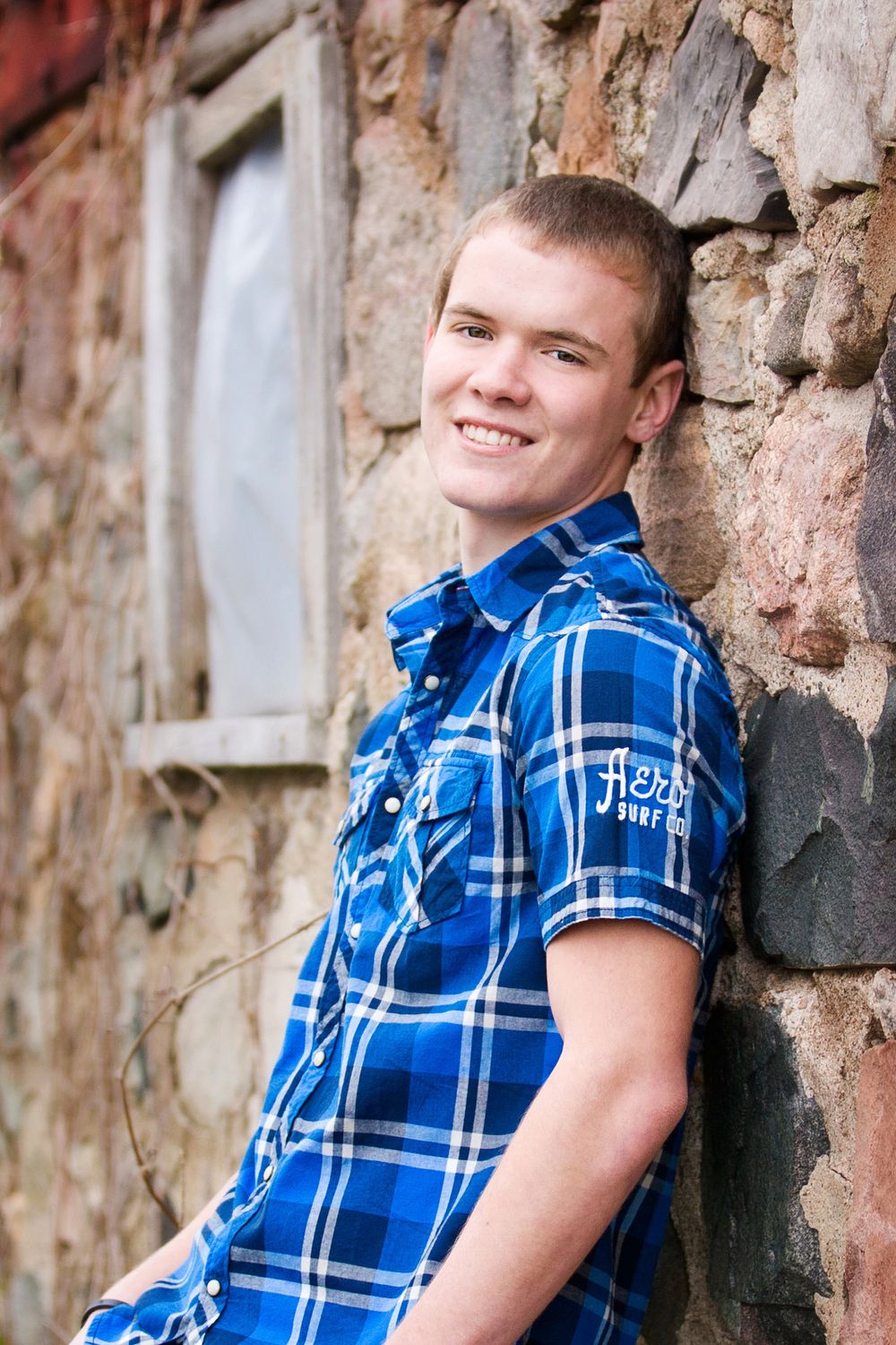 High school senior photo of boy close up with farm cottage brick; portrait session in Howell, Michigan by Brighton, MI photographer