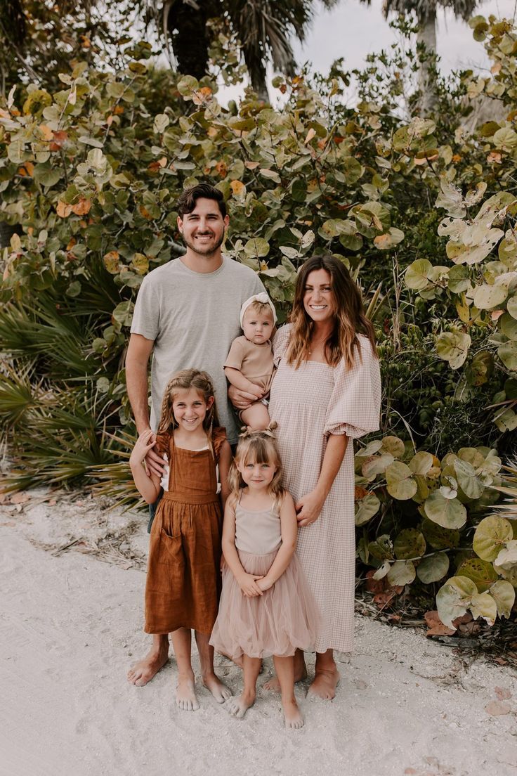 A family standing together outdoors against a backdrop of lush tropical foliage wearing coordinated neutral tones.