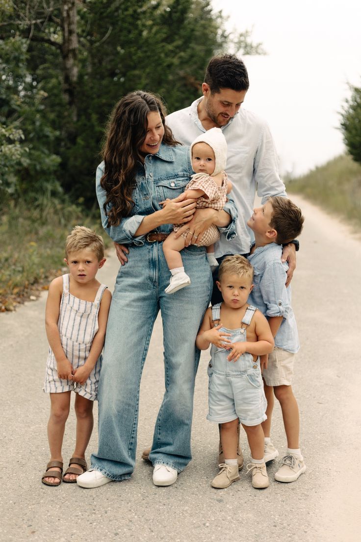 A family wearing coordinated denim and neutral outfits poses together on a gravel path surrounded by greenery.