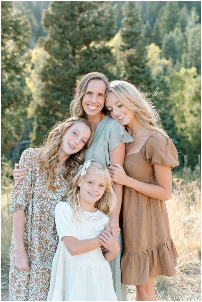 A group hugs and smiles together while posing for a portrait in front of a forested mountain backdrop.