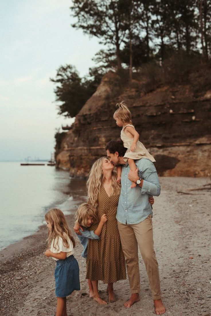 Family stands together on beach at sunset with rocky cliffs and water in background.