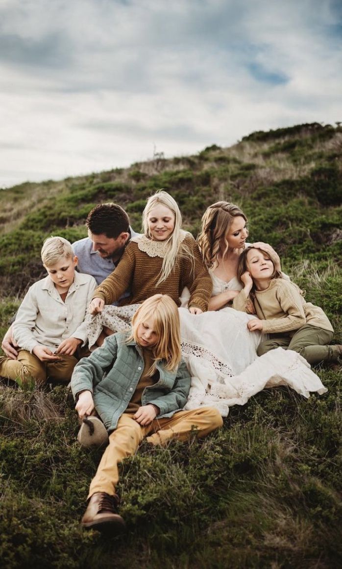 A group relaxes together on a grassy hillside wearing coordinated earth-toned outfits on an overcast day.