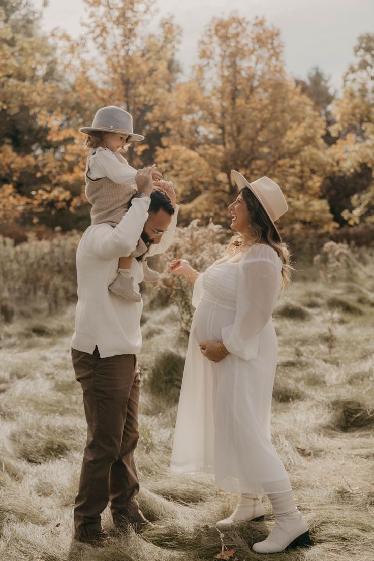 Sweet family moment captured in golden fall setting with matching neutral outfits and hats in a dreamy field.