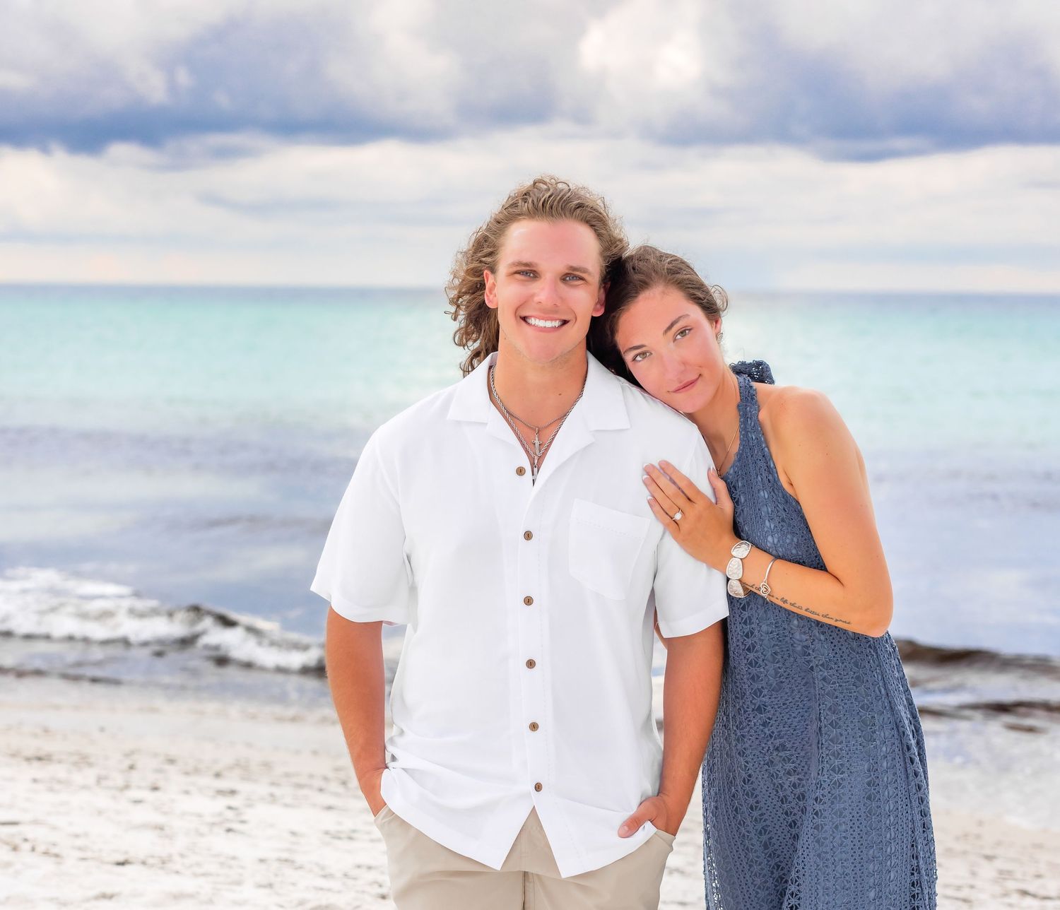 A relaxed couple strolls along a white sandy beach with crystal clear turquoise waters in the background.