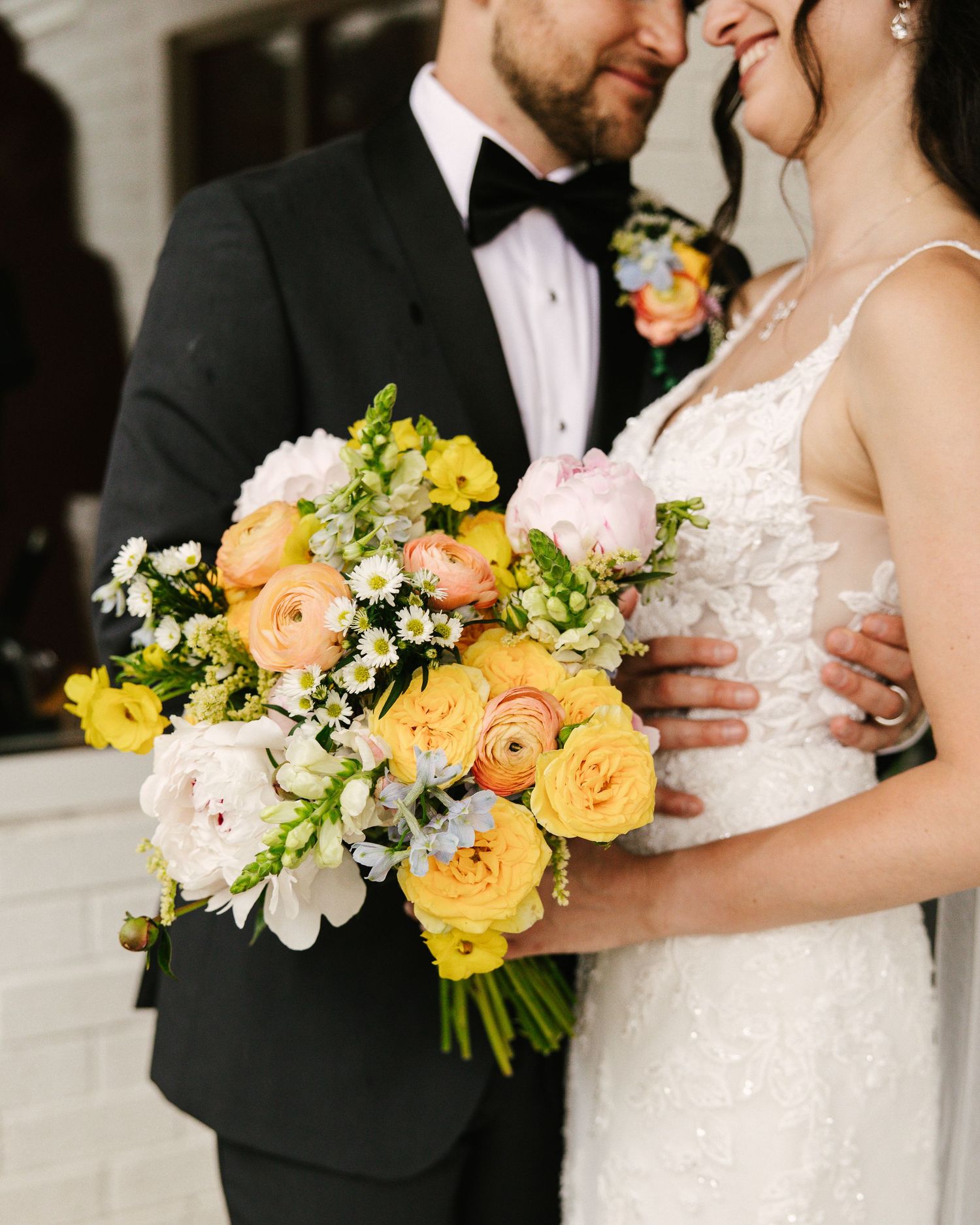 Wedding couple poses with vibrant yellow and peach floral bouquet.