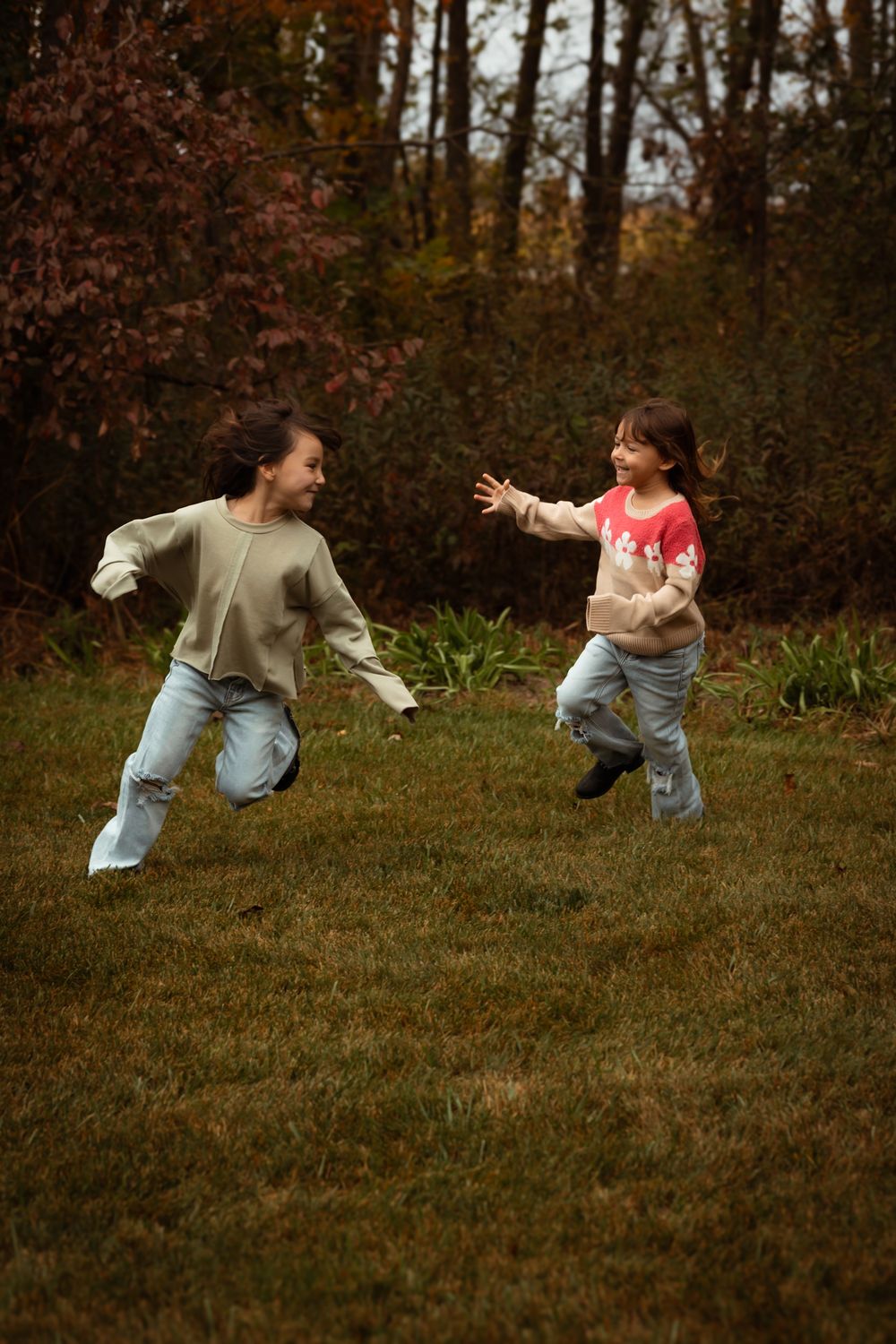 Two people playfully chase and jump after a white bird on a grassy lawn during autumn.