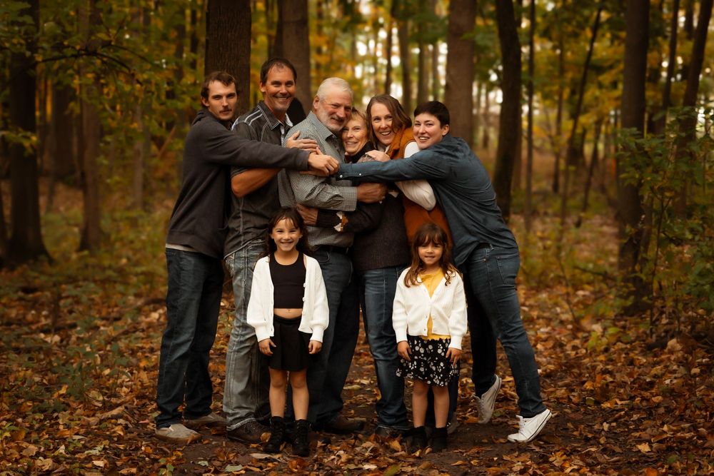A family shares joyful moments together during an autumn photoshoot in a wooded area with fallen leaves.