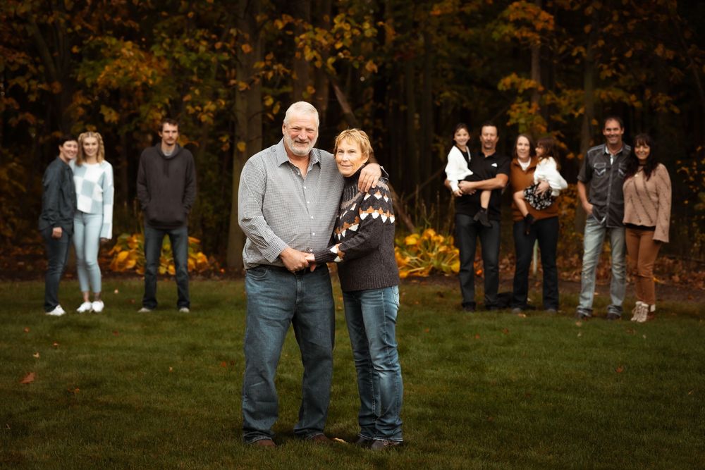 A group enjoys a festive autumn gathering outdoors with golden trees and fallen leaves in the background.