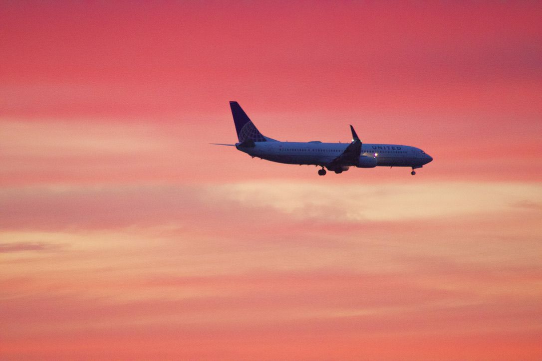 Commercial airplane silhouetted against a vibrant pink and orange sunset sky.