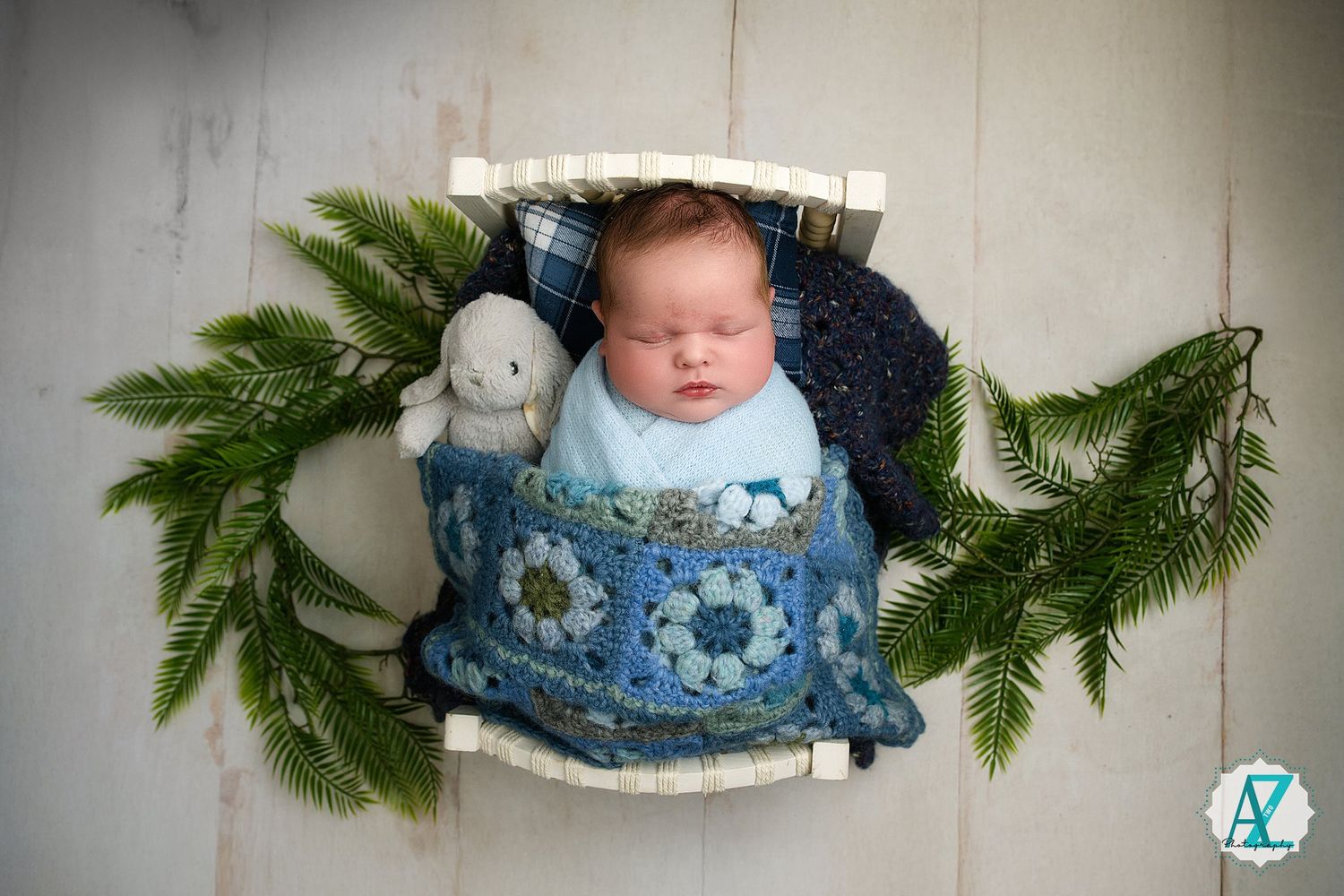 Series of professional newborn photography shots featuring a rustic wood prop with evergreen branches and blue fabric.