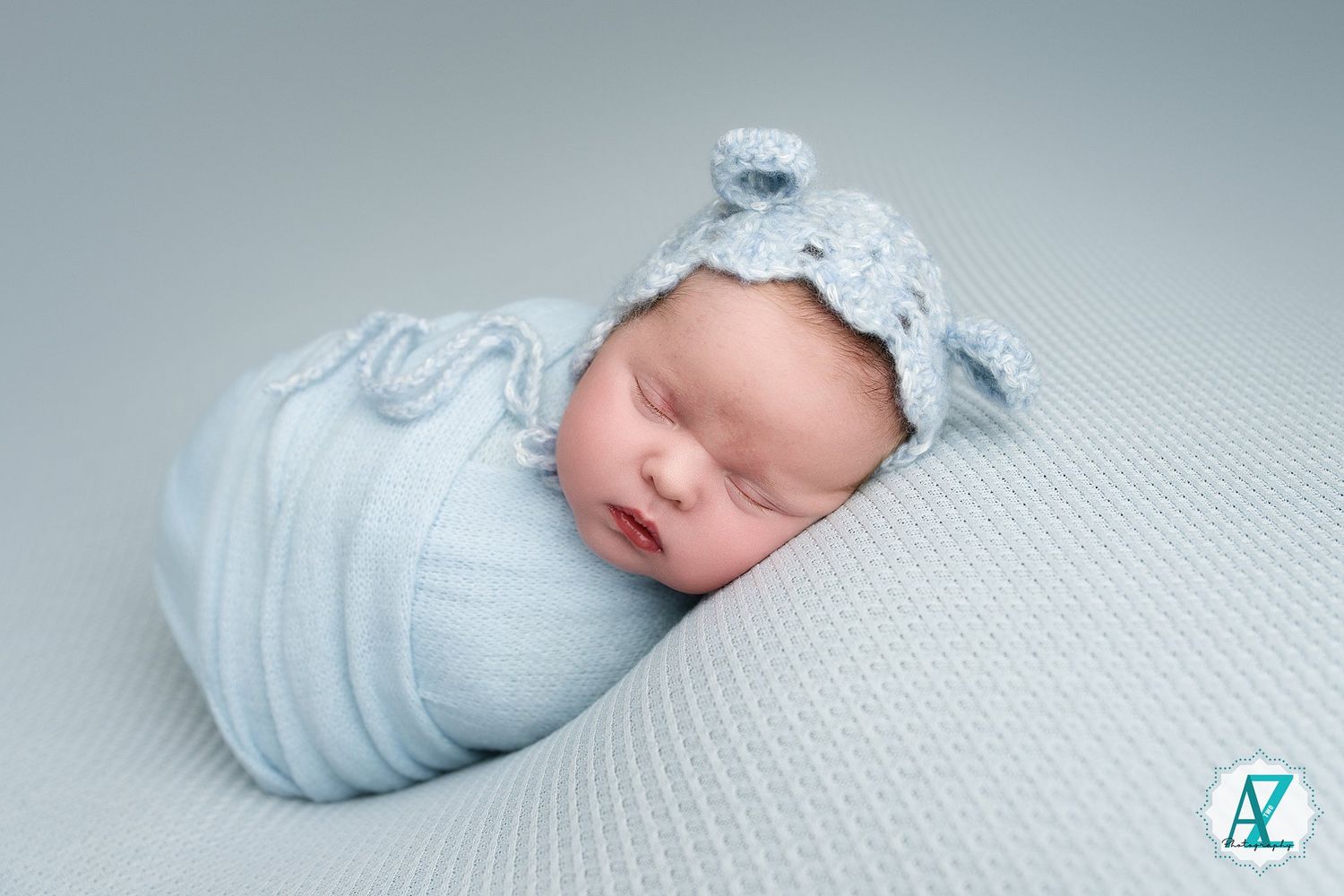 Baby dressed in light blue sleepwear resting on textured white bedding.