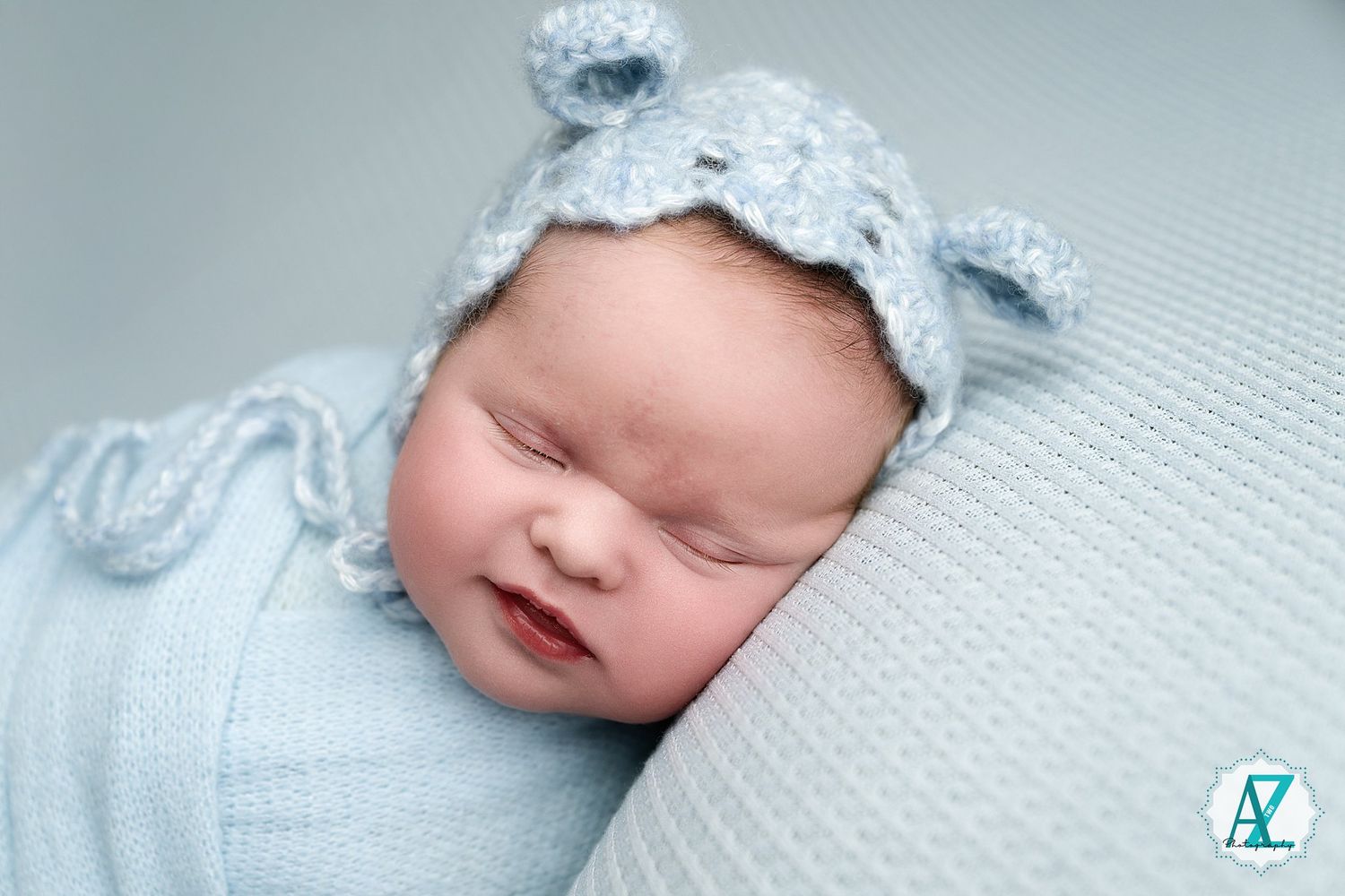 Close-up of sleeping newborn in soft blue wrap on textured white background.