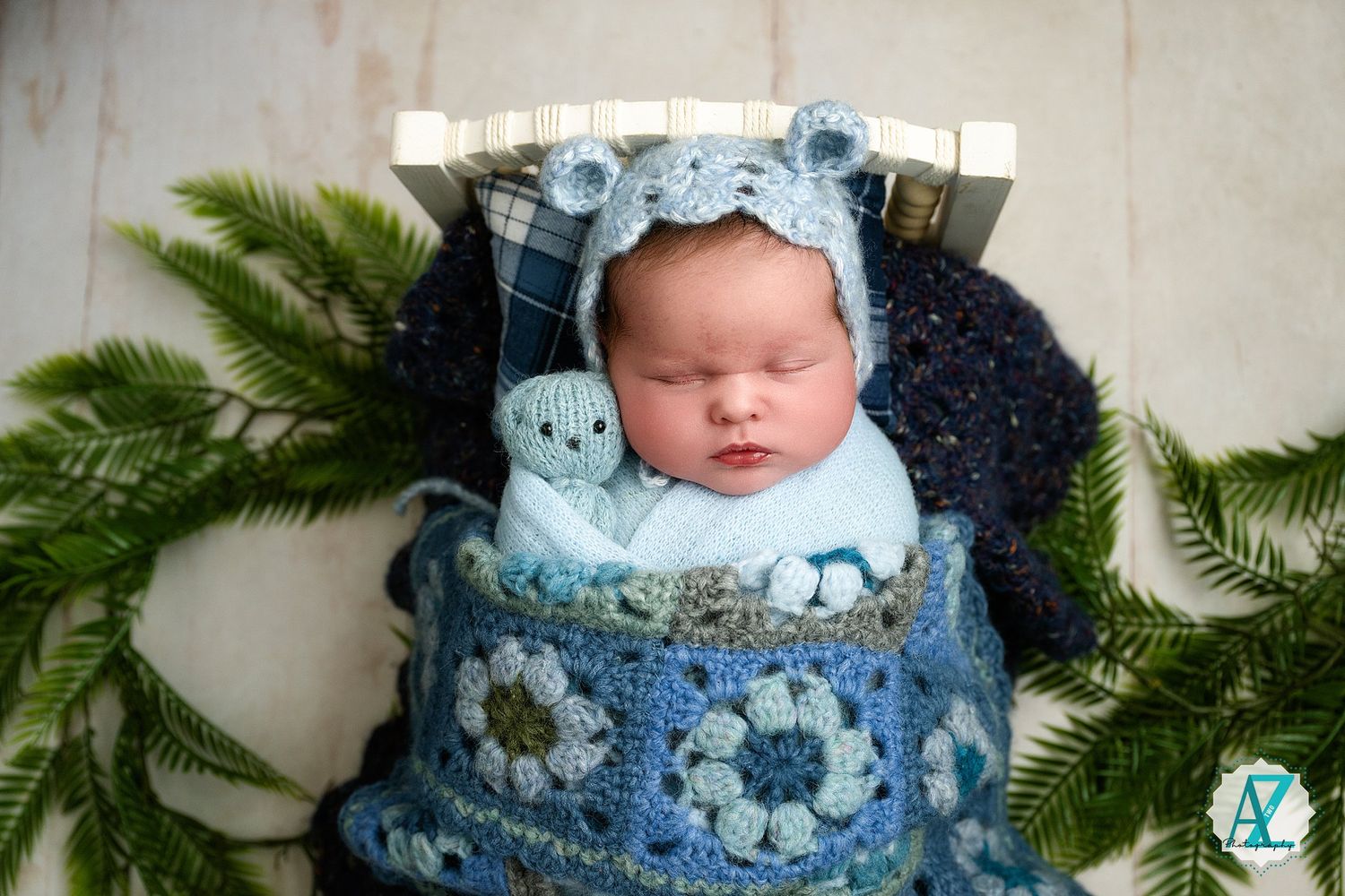 Newborn photography with blue floral wrap and evergreen branches in natural light setting.